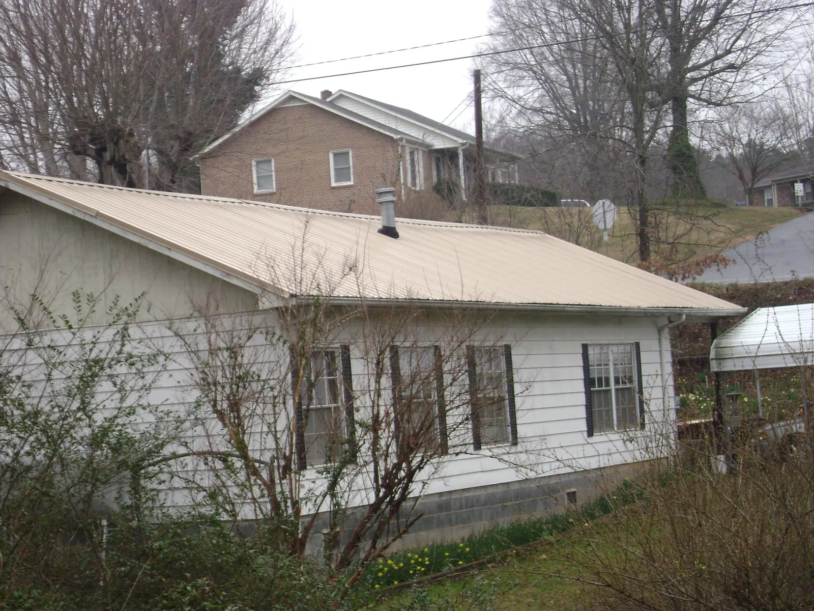 Tan metal roof on a white sided house set into a hillside — Commercial Roofing by Roofing Brothers in Melbourne